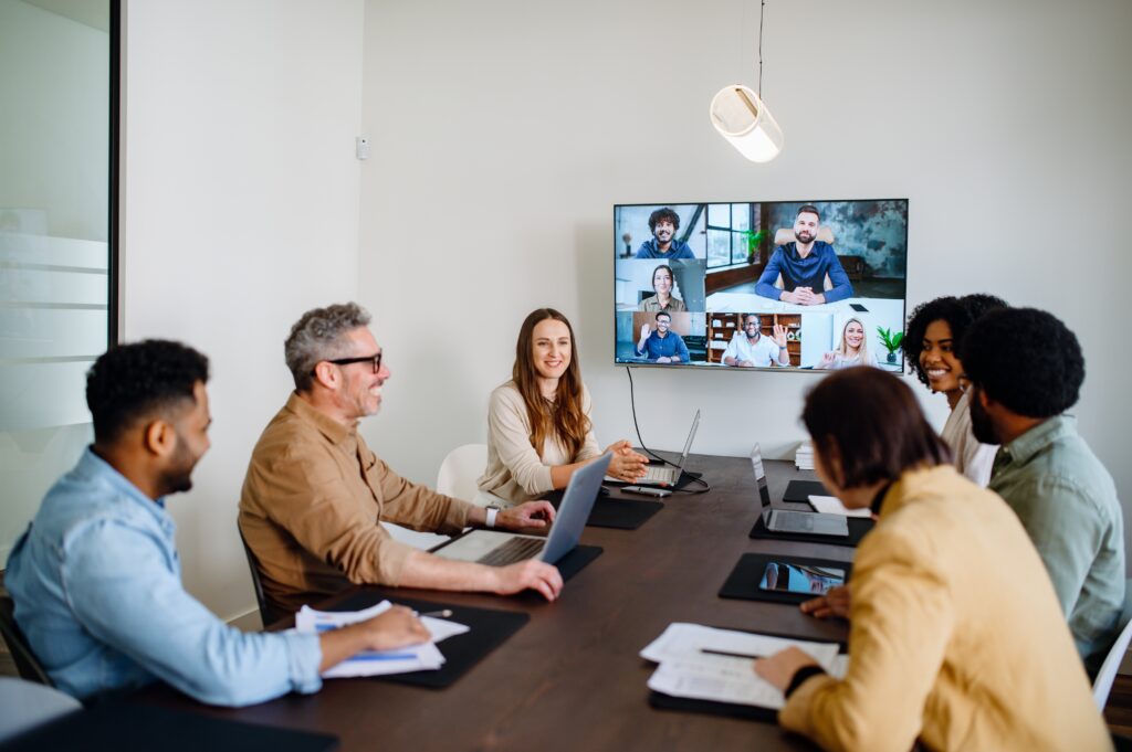 A team meeting where colleagues are connected via a large screen, showcasing a blend of in-person and remote collaboration.