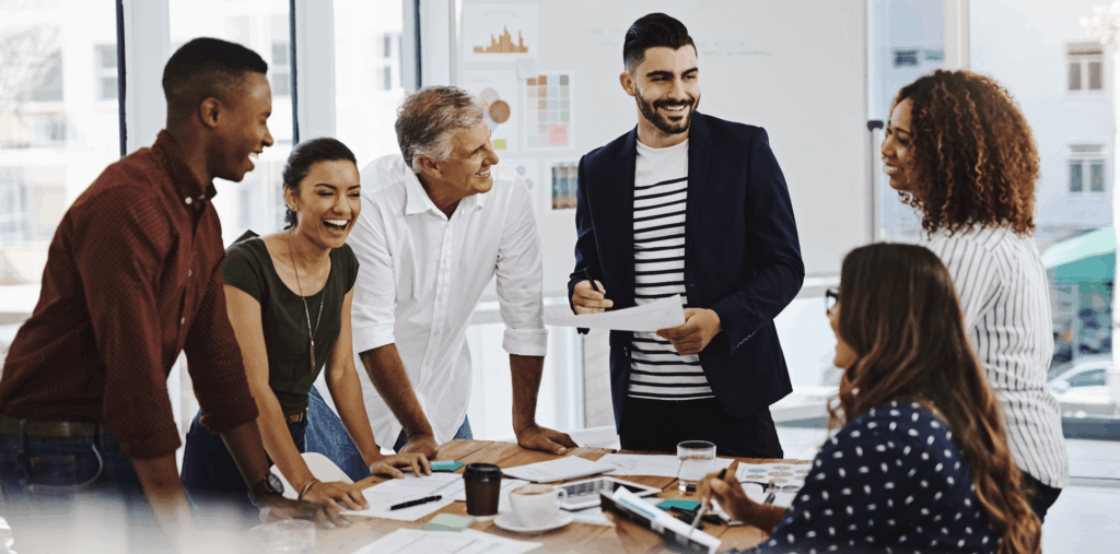 A diverse workforce gathered around a board table smiling.
